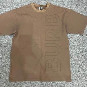 Brun t-shirt med text - Snygg brun t-shirt från Burberry med stor text på både fram- och baksidan. Den har en klassisk rund hals och korta ärmar. Perfekt för en avslappnad stil.