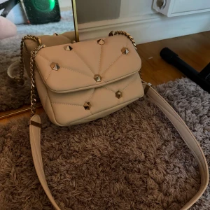 Beige axelväska med nitar - Snygg beige axelväska med guldfärgade nitar och kedjedetaljer från Zara som aldrig använts. Väskan ett praktiskt innerfack. Gullig väska som passar till mycket💛🤍