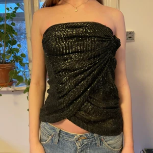 Tubtopp med paljetter - Cool svart tubtopp med grönaktiga paljetter och omlått detalj. Toppen är axelbandslös och har en dragkedja på sidan! 🪲🪐💚