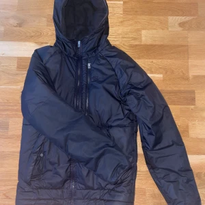 Nike jacka - Säljer en svart Nike Therma-Fit jacka med huva och dragkedja. Jackan har broderad logga på bröstet och praktiska fickor med knappar. Perfekt för kyligare dagar.