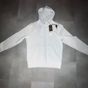 Vit hoodie från BOSS - Säljer en stilren vit hoodie från BOSS helt oanvänd med prislappen kvar,Priset kan diskuteras.