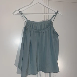 Turkos topp med med rosett  - Snygg turkos topp med smala justerbara axelband och knytning vid halsringningen. Sitter superfint på!