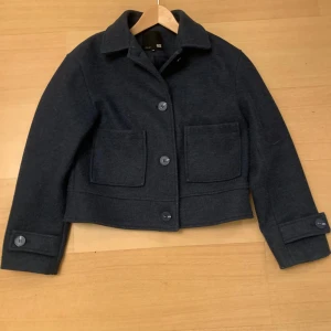 Mörkblå kappa från lager 157 - Snygg mörkblå kappa från 157 i storlek XS. Jackan har en klassisk design med stora knappar och två framfickor. Perfekt för kyliga dagar med sin stilrena look. Nypris 400kr