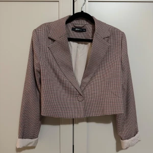 Rutig kavaj från Gina Tricot - Snygg rutig kavaj från Gina Tricot i en croppad modell. Kavajen har en klassisk krage och knäppning framtill. Perfekt för en stilren look. Passar för dom som har xs s 