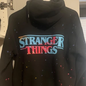 Svart Stranger Things hoodie från Pull&Bear - Cool svart hoodie med Stranger Things-tryck i färgglada nyanser. Framsidan har en bild av karaktärererna från serien. Skriv för frågor och priset kan diskuteras ❣️