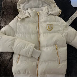 Vit dunjacka med huva - Snygg vit dunjacka med huva och en guldig dragkedja. Jackans färg ser lite annorlunda än på bilden (skulle säga lite gulaktig vit). Storleken är L men passar XXS-S (varnar om att den är väldigt tight vid armarna och väldigt tjock). INTE MIN BILD!! dm för fler bilder och info 💖💋