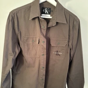 Brun skjorta från Calvin Klein Jeans - Snygg brun skjorta från Calvin Klein Jeans i regular fit. Skjortan har långa ärmar och två bröstfickor med knappar. Perfekt för en stilren look.nypris 800kr