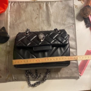 Svart axelväska från Kurt Geiger - Snygg svart axelväska från Kurt Geiger med quiltad design och kedjeaxelrem. Väskan har en dekorativ detalj på framsidan och stängs med magnetlås. Bra skick💗