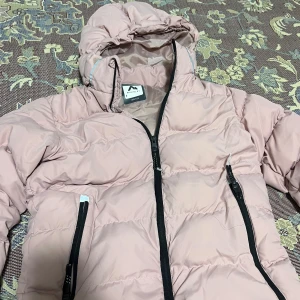 Rosa pufferjacka med huva - Säljer en rosa pufferjacka från Stadium. Bra skick använd ca 7-9 gånger. Värmer jätte bra på vintern och den är väldigt skön att ha på sig!
