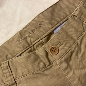 Beige chinos från Boomerang - Snygga beige chinos från Boomerang med klassisk design. Byxorna har en knappgylf och flera praktiska fickor. Perfekta för en stilren look.