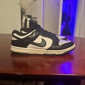 Nike Dunk black/white - Snygga Nike Dunk i svart och vitt med klassisk design. Skorna har snörning och en låg profil som passar perfekt för en avslappnad stil. Perfekta för sneakerälskare som vill ha en tidlös look.