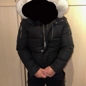 Moose knuckles vinterjacka herr - Snygg svart dunjacka från Moose Knuckles med pälsdetaljer på huvan. Jackan har dragkedja och knappar framtill samt långa ärmar med dragkedjor vid ärmsluten. Perfekt för kalla vinterdagar. Används under en vinter
