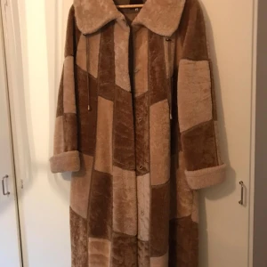 Brun och beige pälsjacka - Säljer en unik brun och beige pälsjacka med patchwork-design. Jackan har långa ärmar och en stor krage. Perfekt för att hålla sig varm och stilren under kalla dagar.