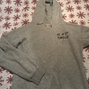 Grå hoodie med text - Säljer en grå hoodie med texten 'JE M'EN AMOUR' och en stjärna tryckt på både framsidan och baksidan. Storleken är 146/152 men är oversize så passar även till 158