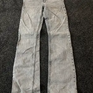 Säljer ett par grå jeansbyxor med hög midja och bootcut-stil. 