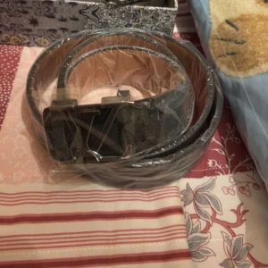 Svart bälte med spänne - Snyggt svart bälte med ett stilrent spänne. Perfekt för att komplettera din outfit. Bältet är inslaget i plast och ser ut att vara i bra skick.