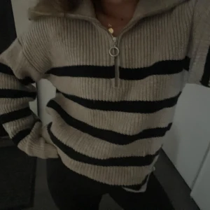 Tröja från Stockh LM - Säljer en snygg beige tröja med svarta ränder från Stockh LM. Tröjan har en dragkedja framtill och är ribbad i materialet. Perfekt för en stilren look. (Storlek XS men S funkar oxå, beror på hur man vill ha den) ordinarie pris 899
