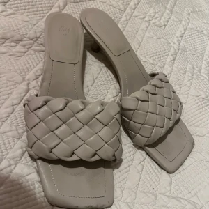 Beige/grå flätade sandaler med klack - Säljer ett par snygga beige sandaler med flätad design och låg klack. Perfekta för sommaren och passar både till vardags och fest. De har en fyrkantig tå och är i mycket bra skick. Superbekväma och stilrena! Klacken är 1-2 cm bara
