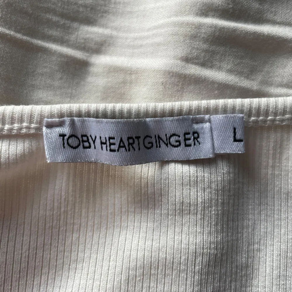 Säljer en superfin vit ribbad topp från Toby Heart Ginger. Den har en söt rynkad detalj framtill och korta ärmar. Perfekt för en somrig dag! 🕊️. Toppar.