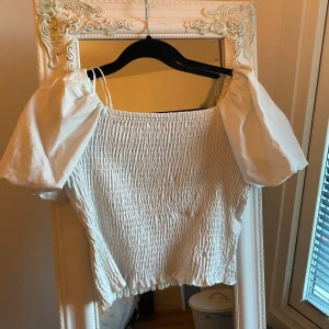 Vit smockad topp från Gina Tricot - Säljer en superfin vit smockad topp från Gina Tricot i storlek S. Toppen har korta puffärmar och en elastisk smockad design ❤️