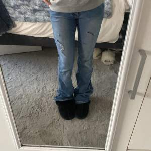 Säljer ett par snygga blå bootcut jeans i bra skick. De har en cool slitning på framsidan och är perfekta för en avslappnad stil. Jeansen är lågmidjade och passar perfekt till både vardag och fest. Sköna och trendiga! Midjemåttet är 33 och Innerbens längden är 83,5