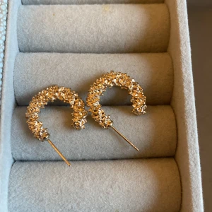 Guldglittriga örhängen - Säljer ett par fantastiska guldglittriga örhängen i form av halvcirklar. De är täckta med små glittrande detaljer som ger en lyxig känsla. Perfekta för att lysa upp vilken outfit som helst, oavsett om det är till fest eller vardag. Passar perfekt för jul och nyår!