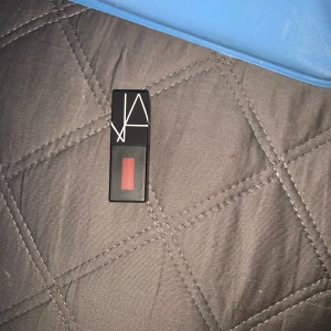 Sminkprodukter till salu - Säljer ett set med sminkprodukter. Inkluderar ett rött läppstift från NARS, en brun läppenna från Milani och en ögonskuggspalett från IsaDora med fyra nyanser i brunt och beige. Perfekt för en naturlig look eller en mer dramatisk stil. Allt är i bra skick och redo att användas!