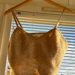 Beige ribbad linnetopp från H&M - Säljer en superfin beige ribbad linnetopp från H&M. Den är croppad och har smala axelband, perfekt för sommardagar eller som ett lager under en kofta. Toppen är i mycket bra skick och gjord av mjukt material som känns skönt mot huden.