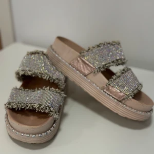 Glittriga sandaler med pärlor - Snygga sandaler med två breda remmar täckta av glittriga paljetter och pärlor. De har en bekväm platt sula och en ljusrosa bas. Perfekta för att lysa upp vilken sommaroutfit som helst! ✨
