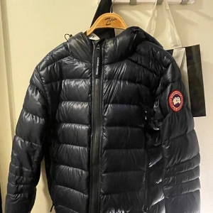 Svart pufferjacka från Canada Goose - Säljer en snygg svart pufferjacka från Canada Goose. Den är perfekt för kalla dagar med sin quiltade design och långa ärmar. Jackan är köpt på johnells och använd fåtal gånger. Digitalt kvitto finns. Pris kan diskuteras och kan även tänka mig byta mot annan jacka! 