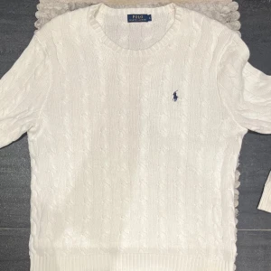 Vit stickad tröja från Polo Ralph Lauren - Säljer en klassisk vit stickad tröja från Polo Ralph Lauren. Den har ett snyggt kabelstickat mönster och den ikoniska loggan broderad på bröstet. Perfekt för både höst och vinter, och den är i mycket bra skick. Passar till alla tillfällen!