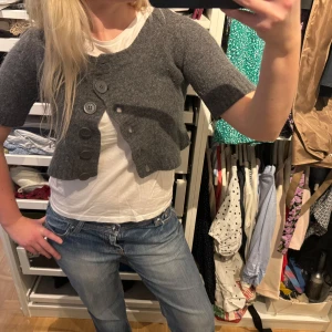 Grå kofta med knappar - Bolero grå kofta med trekvartsärm och stora knappar framtill, står L men kan också bäras i S och M. I mohairmsterial!