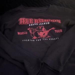 Svart långärmad True Religion - Säljer en svart långärmad tröja från True Religion med coolt tryck i rött. Tröjan är i bra skick och har en skön passform. Tröjan är i storlek (6) som motsvarar XXS.Hör av dig vid intresse!