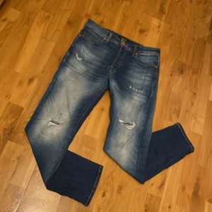 Blå jeans från Jack & Jones - Säljer ett par snygga blå jeans från Jack & Jones i modellen Comfort/Mike. Snygg slitningsdesign (inga hål) och är i väldigt bra skick. Använda i någon vecka, sitter perfekt