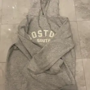 Säljer en grå hoodie med texten 'Boston South' på bröstet. Den är supermjuk och perfekt för kyliga dagar. Har en klassisk känguruficka och en justerbar huva. Perfekt för en avslappnad stil eller mysiga hemmakvällar. 🐨