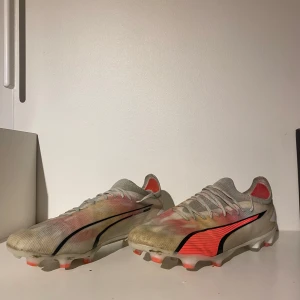 Fotbollsskor Puma ultra  - Säljer ett par fotbollsskor från Puma i bra skick. Skorna är i en vit och röd färgkombination med svarta detaljer. De har snörning och är perfekta för fotbollsträning eller match. Sulan har bra grepp och är designad för att ge stabilitet på planen. Konstgräss och normal gräs