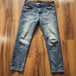 Blåa jeans från Lee - Säljer ett par snygga blå jeansbyxor från Lee. De är regular fit och dom är i bra skick endast använda en gång. Storleken är 33/32