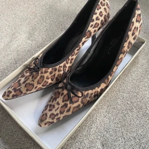 Leopardmönstrade pumps med spetsig tå - Säljer ett par snygga leopardmönstrade pumps med spetsig tå och liten klack. De har en söt rosett framtill och är perfekta för en utekväll eller fest. Skorna är i mycket bra skick och ger en trendig touch till vilken outfit som helst. 🐆✨