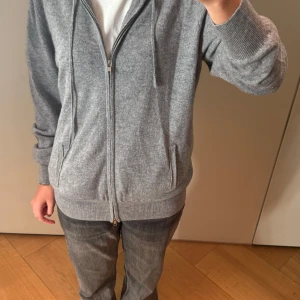 Grå kashmir hoodie från Soft goat   - Mysig grå hoodie från Soft Goat i kashmir. Perfekt för kyliga dagar med dragkedja och fickor framtill. Den har en avslappnad passform och ribbade muddar vid ärmslut och nederkant. Superbekväm och stilren!Koftan är i storlek L men är liten i storleken enligt mig. 