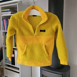 Gul fleece från Peak Performance - Säljer en supermysig gul fleece från Peak Performance i storlek 150. Perfekt för kyliga dagar med sin halvdragkedja och praktiska magficka. Den är i mycket bra skick och redo för nya äventyr! 💛
