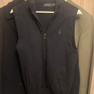 Blå knitted väst från Polo Ralph Lauren storlek S - Säljer en stilren mörkblå väst från Polo Ralph Lauren i storlek S. Västen har en dragkedja framtill och är perfekt för lager-på-lager under höst och vår. Den är i mycket bra skick och har en liten broderad logga på bröstet. Passar både till vardags och fest. Sälja för 2000 på nätet så jag tycker detta är en väldigt bra deal :)