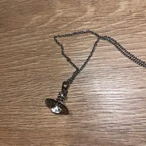 Säljer ett coolt silverfärgat halsband från Vivienne Westwood. Det har en unik berlock formad som en planet med en klar sten i mitten. Perfekt för att ge din outfit en edgy touch. Kedjan är i bra skick och har en liten märkestagg.