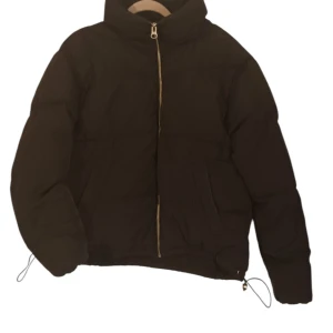 Svart pufferjacka från Divided - Säljer en svart pufferjacka från Divided i storlek M. Jackan har en dragkedja framtill och justerbar dragsko i nederkanten för extra värme. Perfekt för kyliga dagar med sin vadderade design. Tillverkad i 100% polyester.