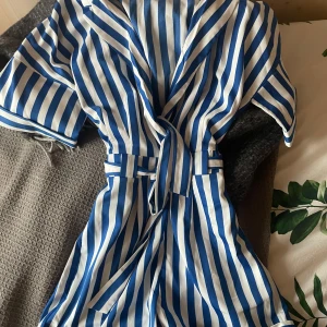 Randig klänning med knytband - Säljer en superfin randig shorts-dress i blått och vitt. Den har ett knytband i midjan och korta ärmar, perfekt för sommardagar. Materialet känns lätt och luftigt! Passar både till vardags och festligare tillfällen!💕💕den är strlk M men skulle säga att den är ganska liten i storleken därför passar den mig som har xs/s.