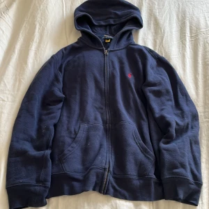 Marinkblå hoodie från Polo Ralph Lauren - Säljer en marinblå hoodie från Polo Ralph Lauren i bra skick. Den har en dragkedja framtill. Perfekt för höst och vinter med sin mysiga fleeceinsida. Passar både till vardags och chillkvällar. 🧥