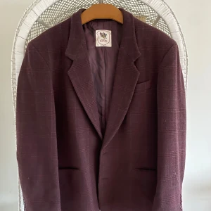 Vinröd kavaj från Emilio Cloud - Säljer en snygg vinröd kavaj från Emilio Cloud i mycket bra skick. Kavajen har ett diskret rutigt mönster och är fodrad med ett slätt tyg. Perfekt för höst och vinter, och funkar både till fest och vardag. Storlek är inte angiven men verkar vara normal passform.