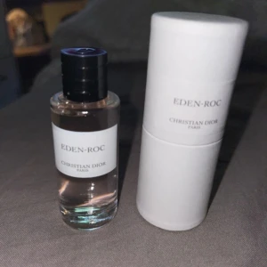 Eden-Roc parfym från Christian Dior - Säljer en elegant flaska av Eden-Roc parfym från Christian Dior. Flaskan är genomskinlig med en svart kork och har en stilren vit etikett. Parfymen kommer i en vit cylinderformad förpackning. Perfekt för den som älskar lyxiga dofter!