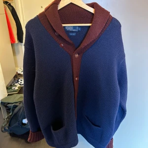 Mörkblå och röd kofta från Polo Ralph Lauren - Säljer en snygg och varm kofta från Polo Ralph Lauren i mörkblått med vinröda detaljer. Den är gjord av 100% ull och har en skön passform med knappar framtill. Perfekt för kyliga höst- och vinterdagar. 🧥Nypris är runt 5-6 k, mitt pris 1599 utöver det är den i toppskick och väldigt trendig just nu. Priset är inte hugget i sten och hör av er vid minsta fundering!👌 