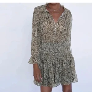 Leopardmönstrad klänning - Snygg leopardmönstrad klänning med långa ärmar och volangdetaljer. Perfekt för en utekväll eller fest! Den har en smickrande passform med elastisk midja och knappar framtill. Materialet är lätt och luftigt, vilket gör den bekväm att bära hela dagen.