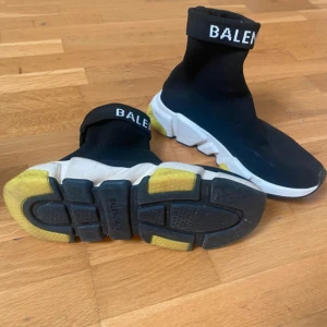 Svarta sneakers från Balenciaga  - Säljer ett par svarta Balenciaga sneakers i storlek 36. De har en strumpliknande design med vit och gul sula. Perfekta för en trendig och bekväm look. Köpt i London på Harrods 